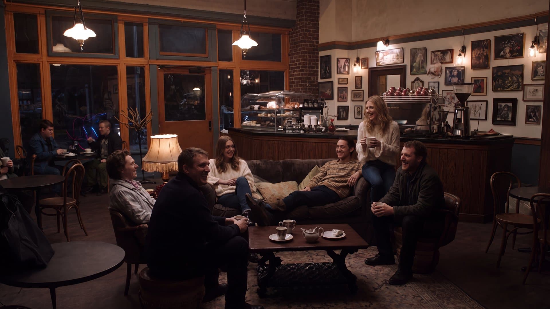 Six friends talking and laughing around the couch of a busy New York coffee house at night.